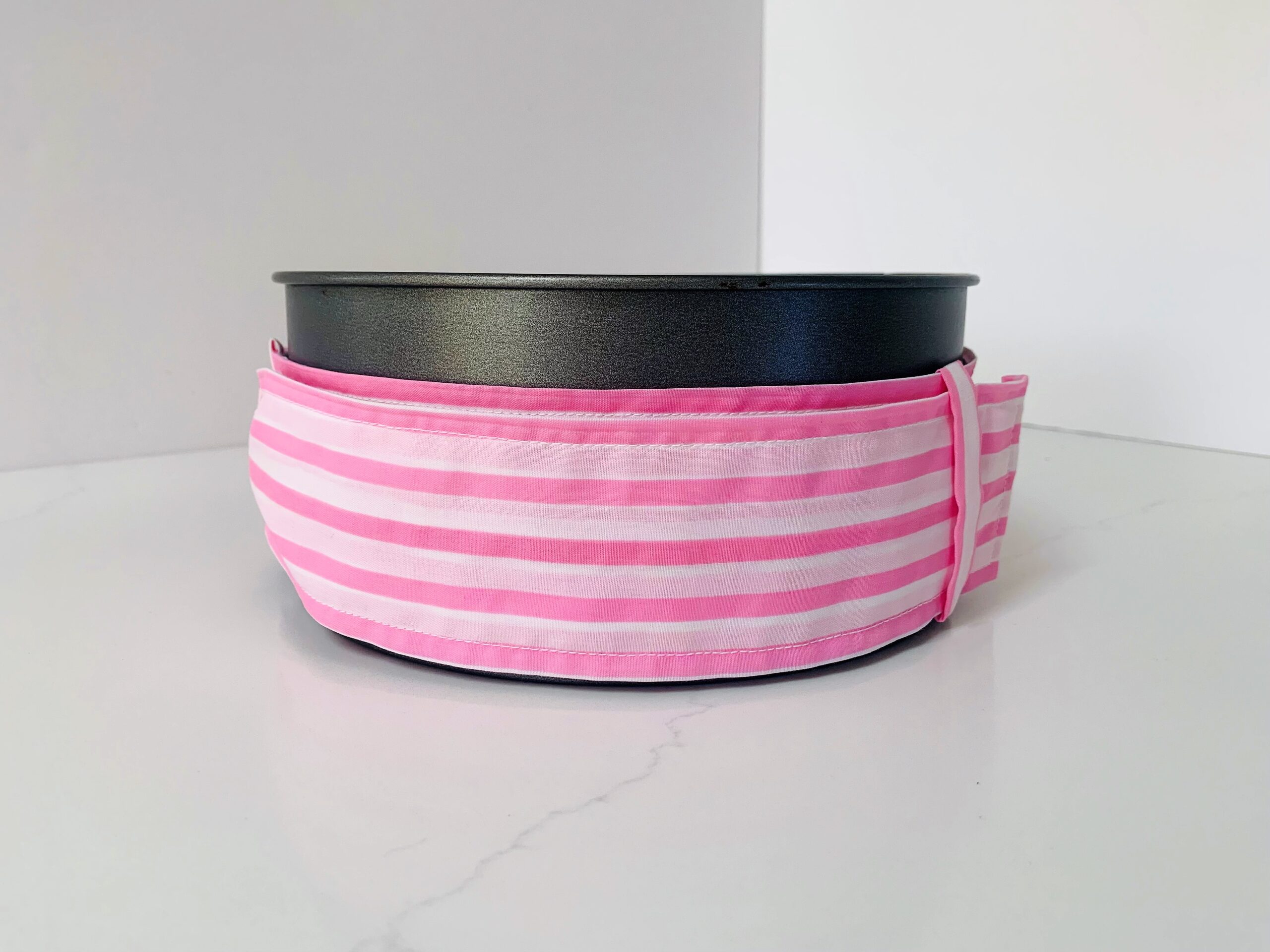 Round baking tin with pink and white stripe baking band around the tin.